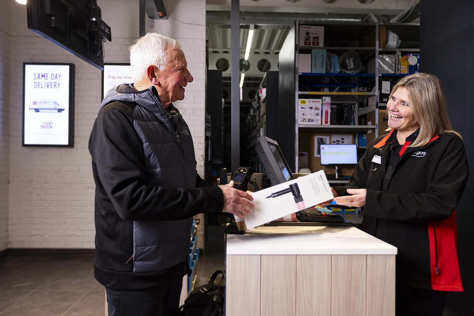 A customer collecting a boxed Dyson hairdryer from an Argos collection counter