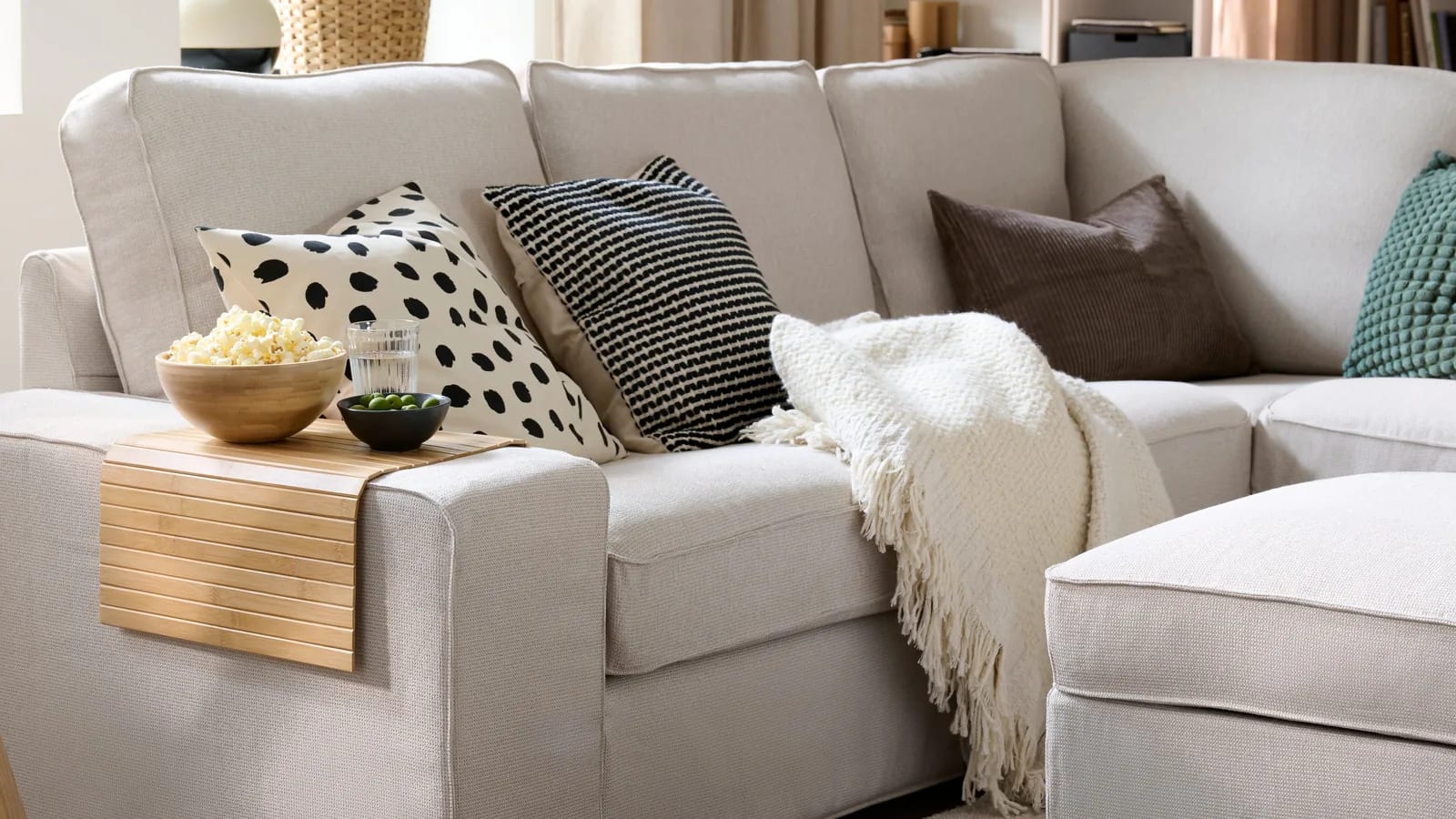 A cream fabric corner sofa styled with cushions and a knitted throw in a bright living room