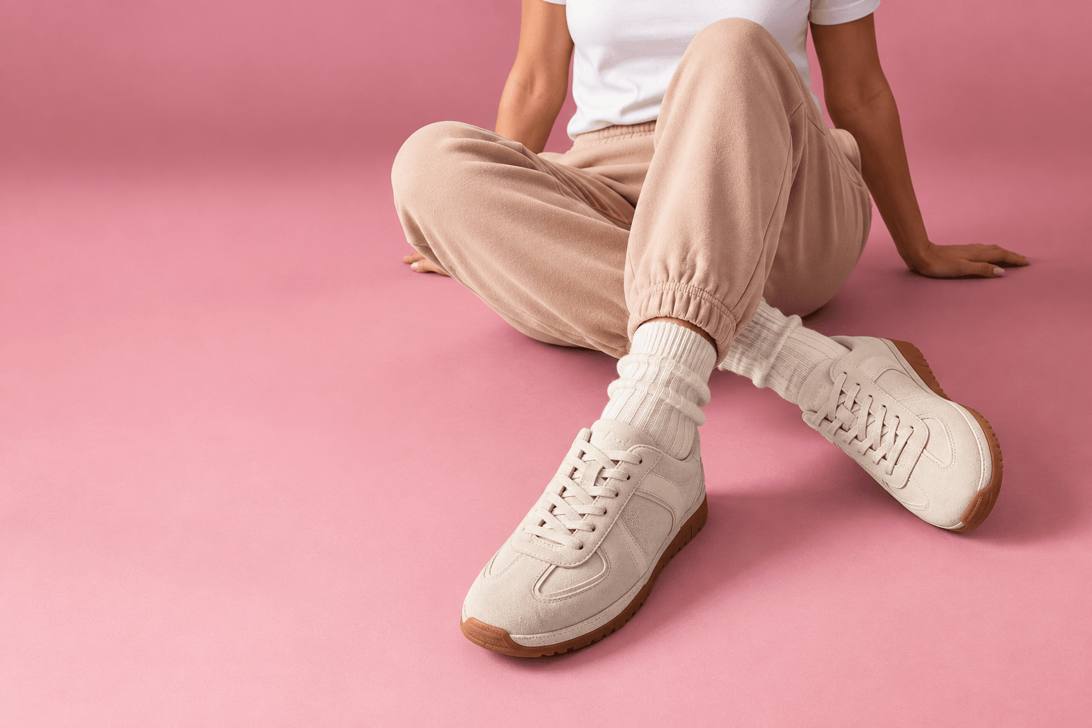 Cream suede trainers on a dusty pink backdrop