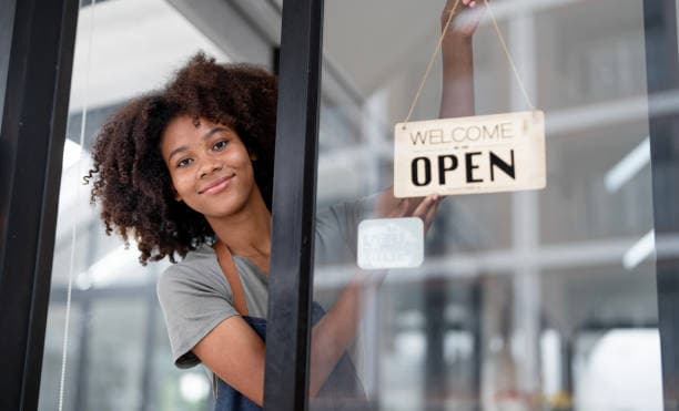 A smiling shop owner hanging a “Welcome, we’re open” sign on her door