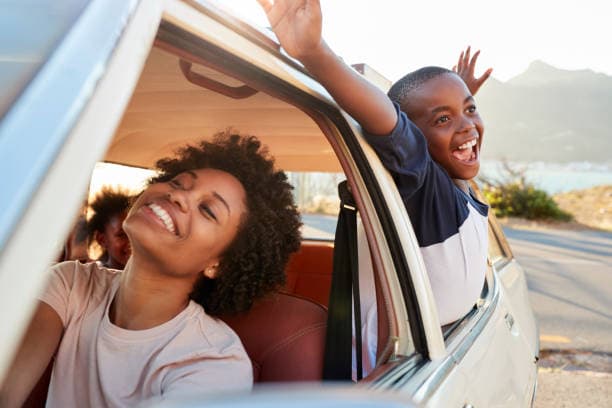 A mother and son smiling out of the windows of a car on a road trip